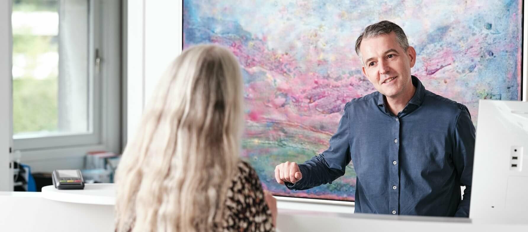 Billedet viser en patientkoordinator, som hjælper en patient ved praktisk info.