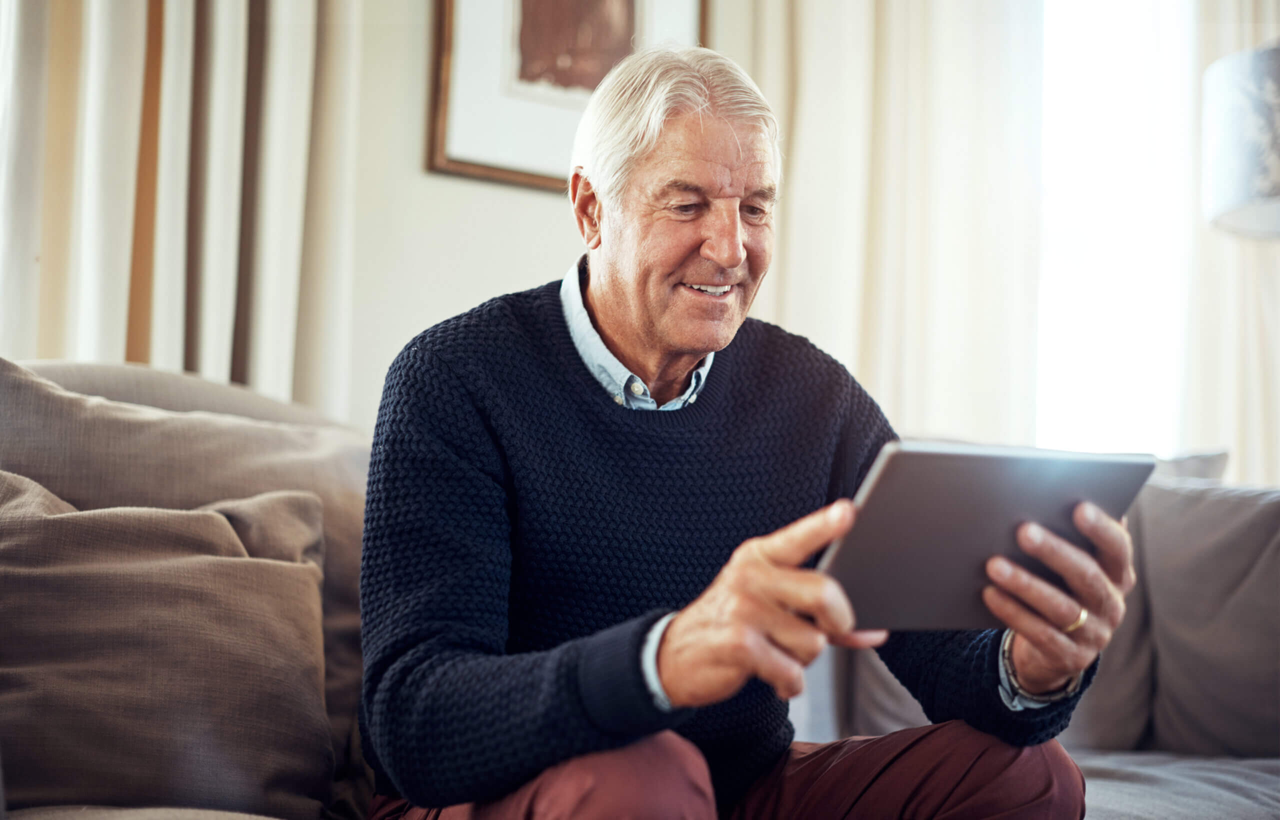 Beskåret billede af en ældre mand, der bruger en digital tablet derhjemme.
