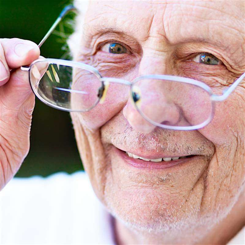 Ældre mand smiler, mens han holder sine briller.